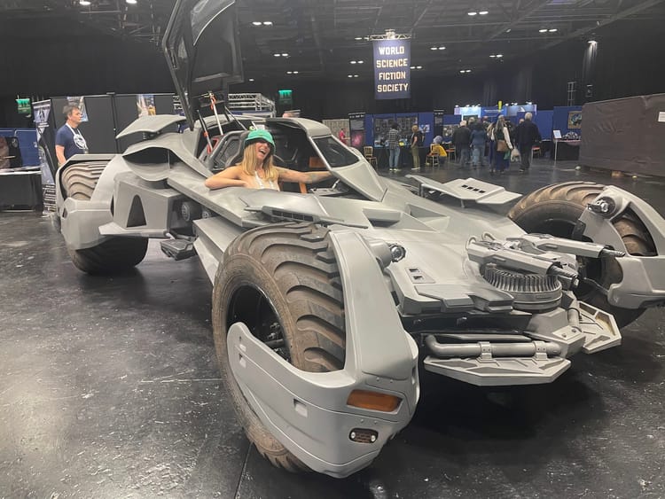 Sam sitting inside a Batmobile wearing a frog hat